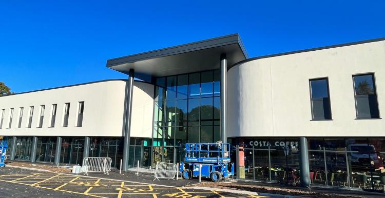 A photograph showing the new front of the hospital. It has a raised overhang supported by pillars, a glass-fronted first floor, and a clean, cladded upper floor. There is a 'Costa Coffee' sign on part of the ground floor