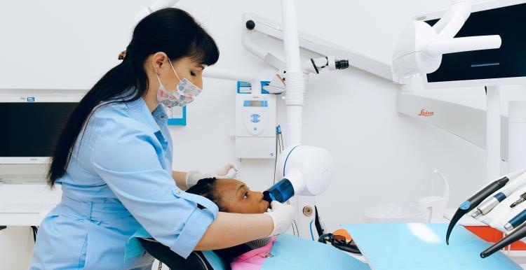 A dentist wearing a facemask leans over a patient in a reclined chair, performing a procedure on their mouth