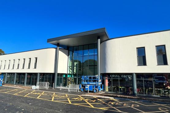 A photograph showing the new front of the hospital. It has a raised overhang supported by pillars, a glass-fronted first floor, and a clean, cladded upper floor. There is a 'Costa Coffee' sign on part of the ground floor