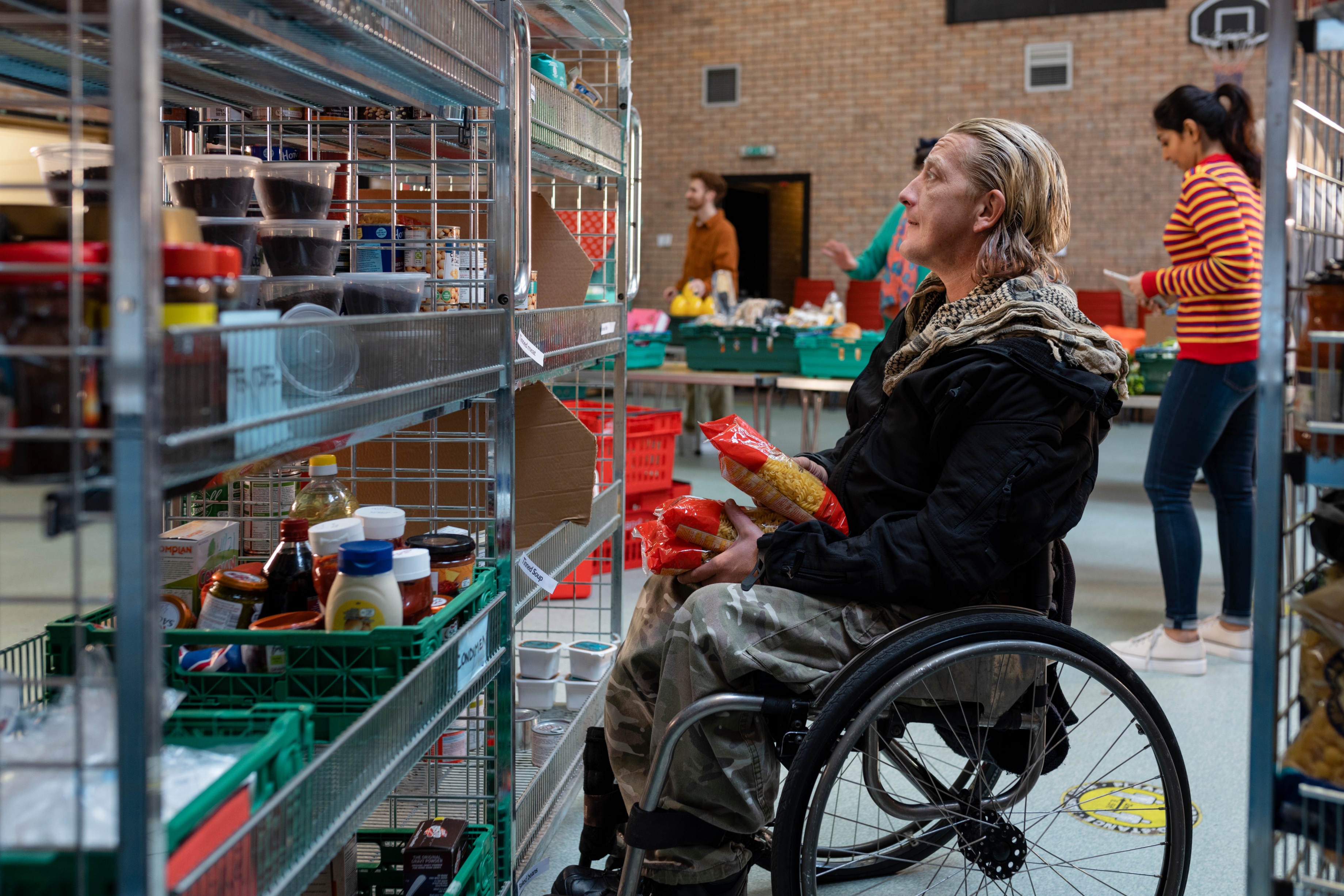 A man in a wheelchair looks up at assorted food items in wire baskets on shelves