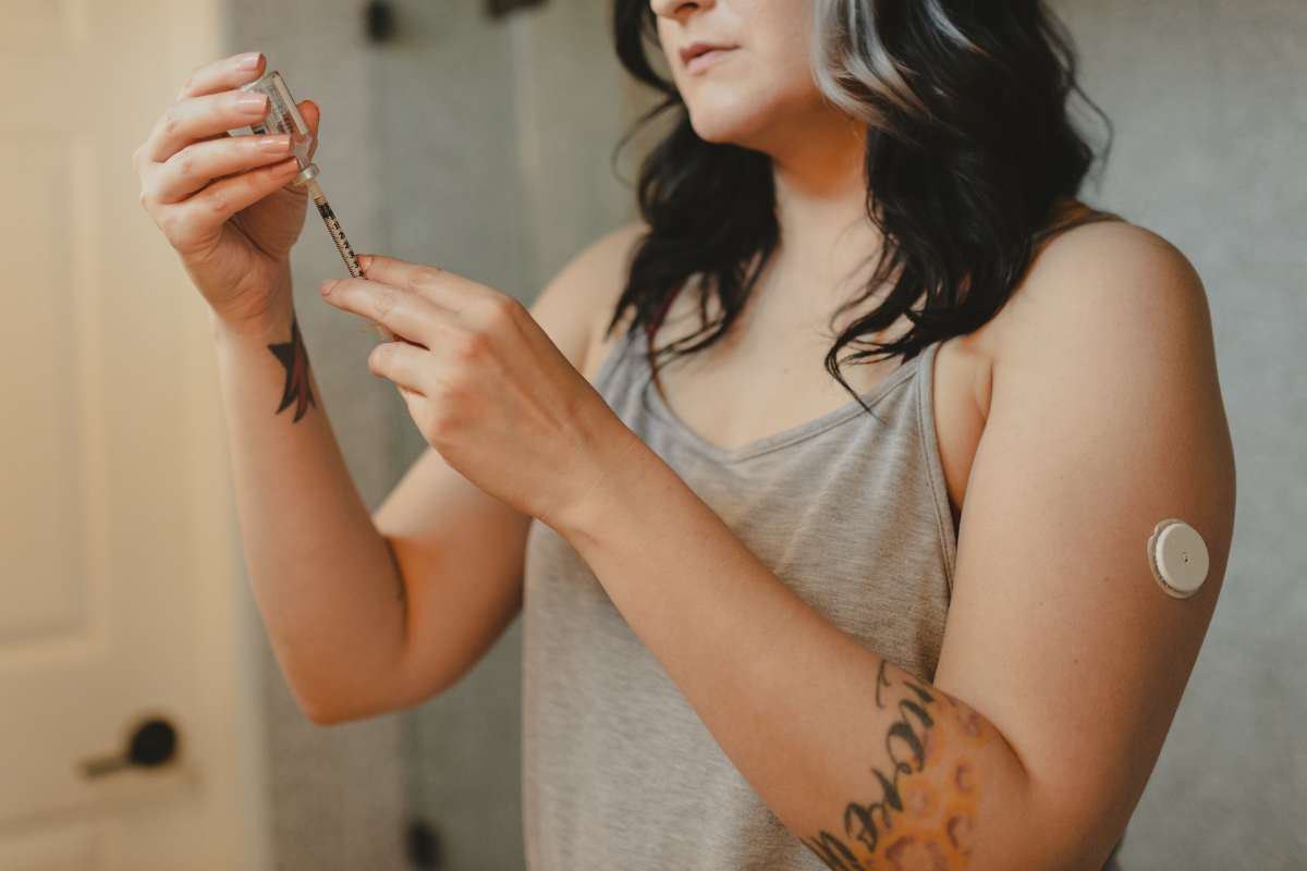 A woman with tattoos conducts a finger pin-prick blood test on her hand