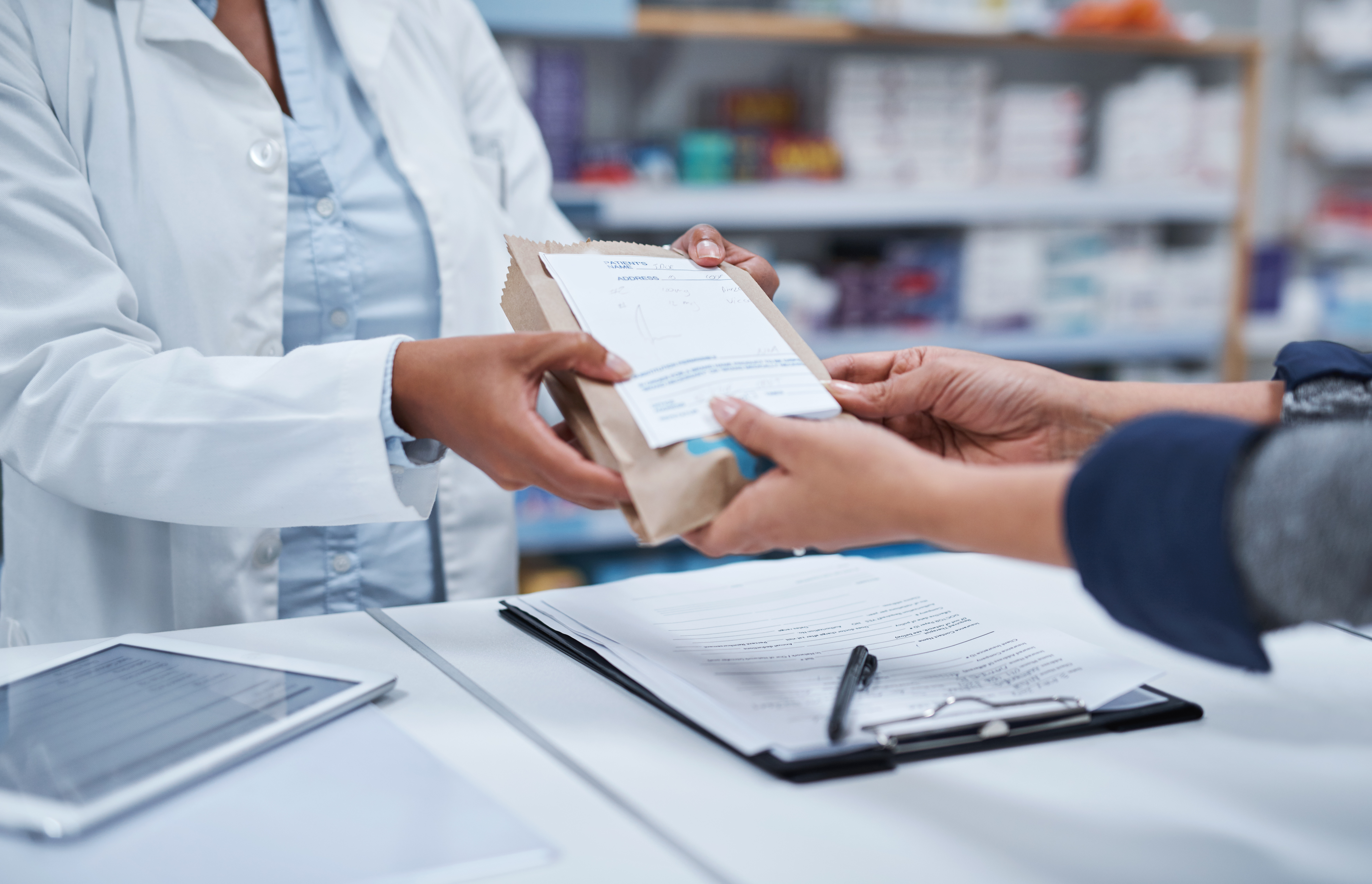 A pharmacist hands over a prescription in a brown bag