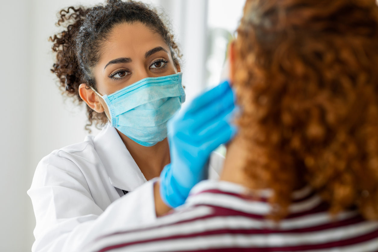 A woman in a labcoat and a surgical mask reaches out