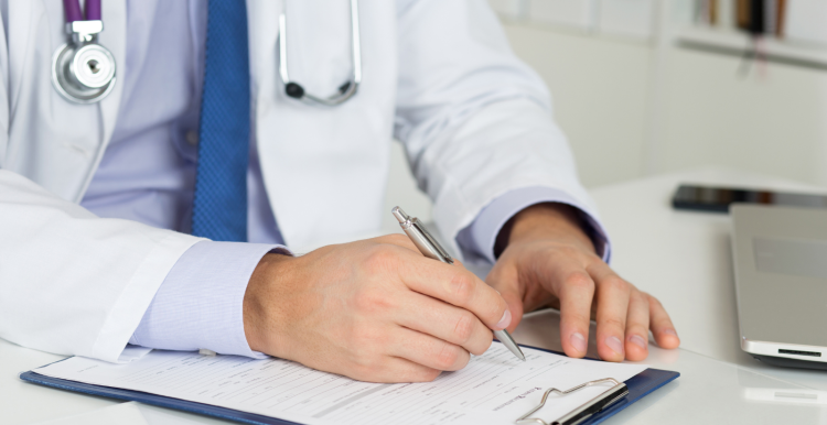 A man in a labcoat and wearing a stethoscope writes something on a clipboard