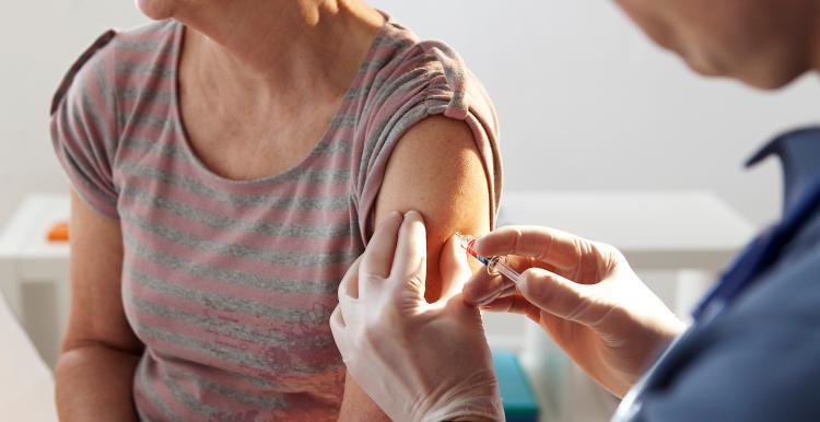 A pair of gloved hands administer a vaccination injection to a woman's arm