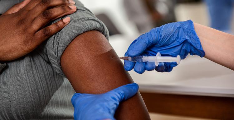 A photograph of a gloved hand administering an injection to someone's arm