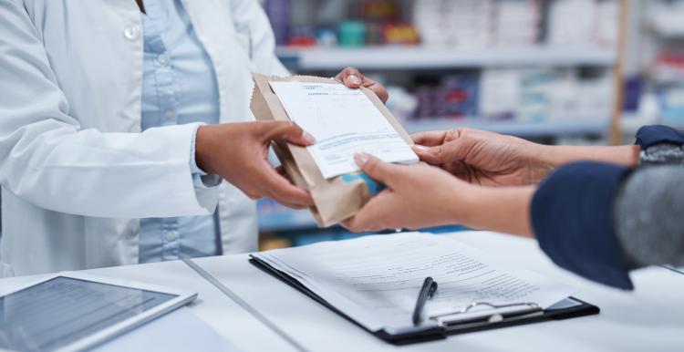 A pharmacist hands over a prescription in a brown bag