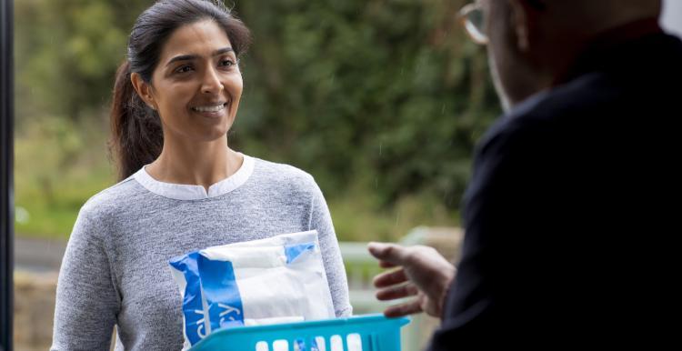 A smiling woman holds a plastic basket with two packages sticking out of it. A man reaches for one of them