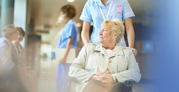 A woman being pushed in a wheelchair by a nurse