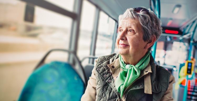 An elderly woman is sitting in a bus, as the scenery blurs out of the window