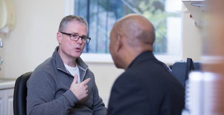 Man sitting in a GP consulting room talking to his male doctor