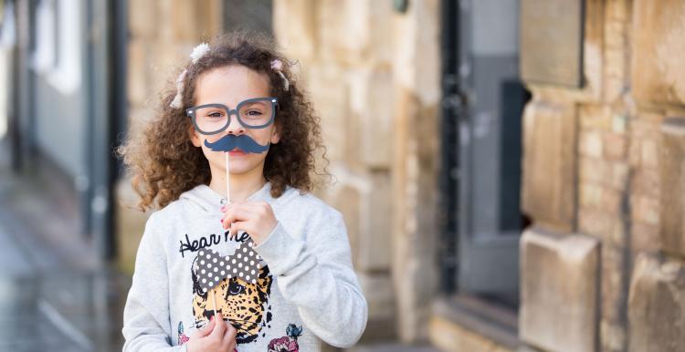 Small child holding up mustache prop for a photograph