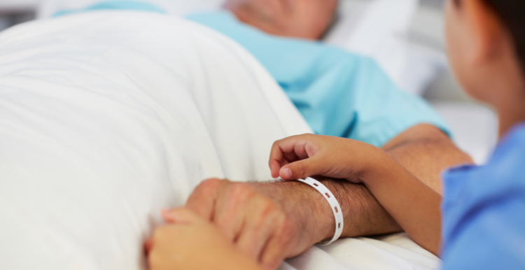 man lying down in a hospital bed with a child holding his hand