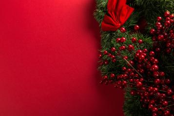 An image depicting some holly with berries and tied bows creeping up the right side of a red background.