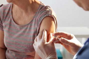 A pair of gloved hands administer a vaccination injection to a woman's arm