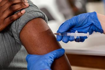 A photograph of a gloved hand administering an injection to someone's arm