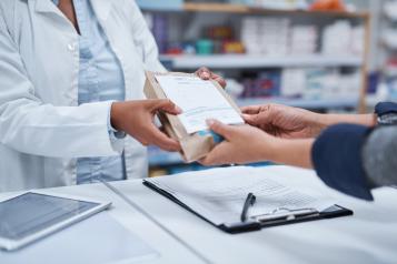 A pharmacist hands over a prescription in a brown bag