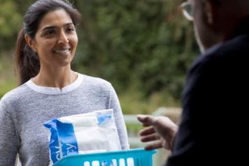 A smiling woman holds a plastic basket with two packages sticking out of it. A man reaches for one of them