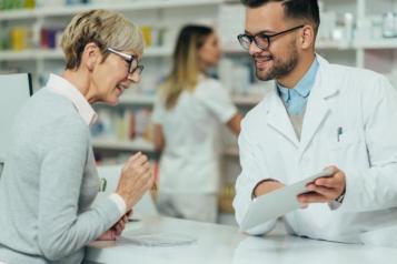 A woman speaks to a pharmacist over the counter, who is showing her a piece of paper