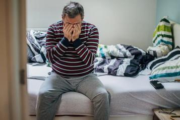 A man sits on an unmade bed, with his hands over his face