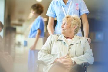 A woman being pushed in a wheelchair by a nurse