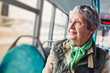 An elderly woman is sitting in a bus, as the scenery blurs out of the window