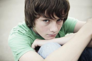 A young boy sitting down hugging his knees