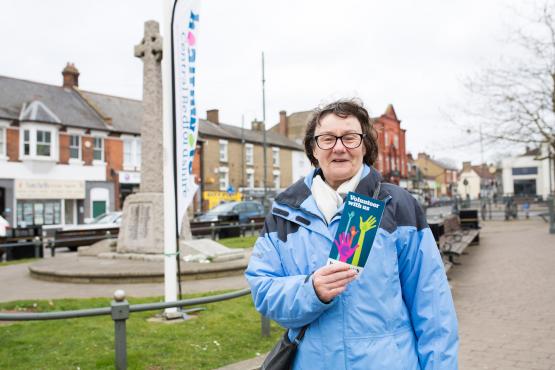 Woman stood outside in her coat holding a leaflet from Healthwatch