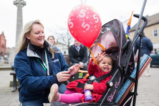 Lady giving a balloon with a number 5 on it to a young child in a pushchair