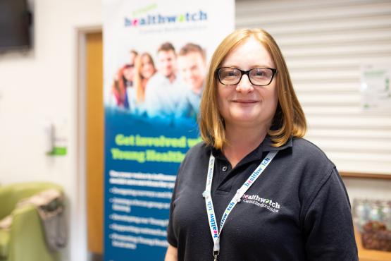 woman in a Healthwatch t shirt standing in front of a Healthwatch flag woman in a Healthwatch t shirt standing in front of a Healthwatch flag