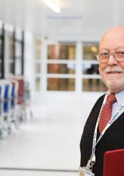 Man in a hospital corridor holding a clipboard